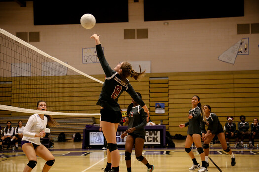 Volleyball player jumping to spike the ball during a competitive match in an indoor gymnasium