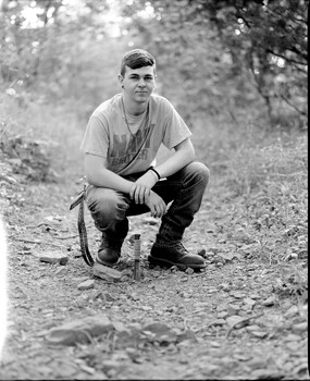 Man in casual clothing crouching on a dirt path with natural foliage in background