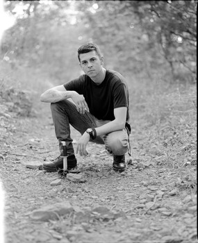 Man in dark shirt crouching on dirt path, black and white portrait