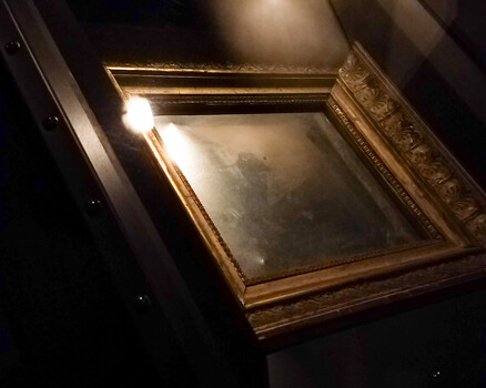 Empty ornate gold frame with glass displayed against dark background with dramatic spotlight lighting
