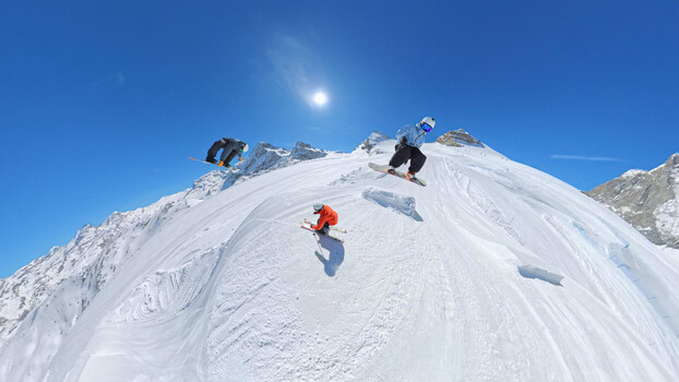 Snowboarders descending a steep snowy mountain slope under clear blue sky