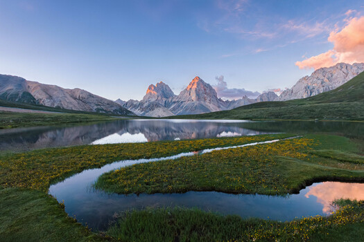 Mountain peaks reflected in curved alpine lake at golden hour