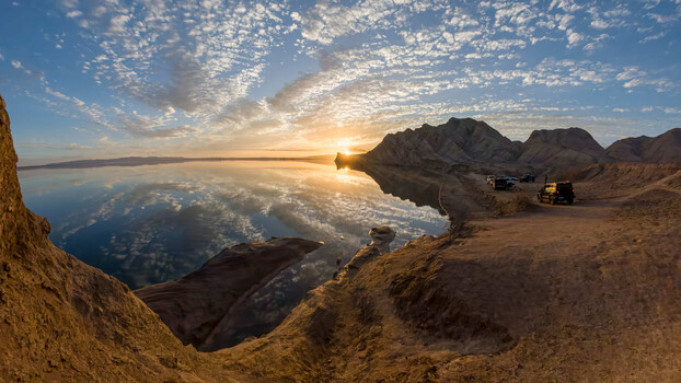 Sunrise over Dead Sea with desert mountains and parked vehicles on sandy overlook