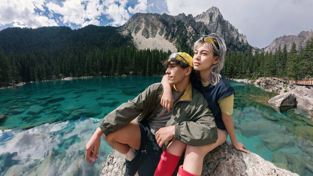 Two people posing on a rock overlooking turquoise alpine lake with dramatic mountain peaks
