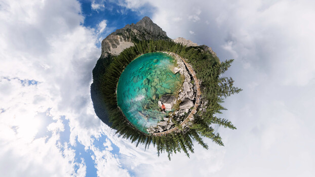 Aerial 360-degree panoramic view of an alpine lake with turquoise water surrounded by dense evergreen forest