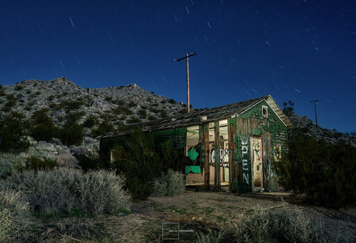 Abandoned desert structure with weathered green wood siding under starry night sky