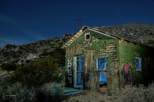 Weathered abandoned structure with green and blue painted wood siding against desert hillside