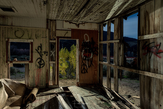 Abandoned interior with open doors framing overgrown landscape and mountains at twilight
