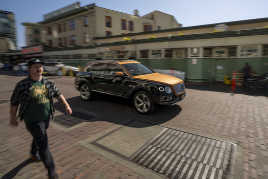 Luxury SUV with two-tone black and gold wrap parked on brick plaza with pedestrians and classical architecture