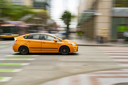 Orange hybrid hatchback in motion blur crossing urban street intersection