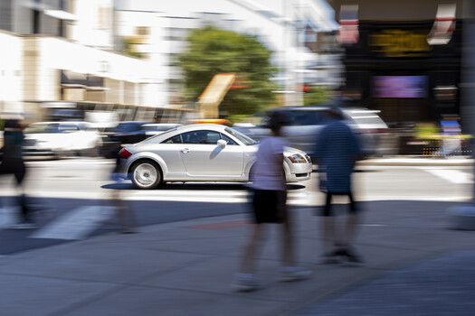 White car with open hood on urban street with motion-blurred pedestrians and buildings