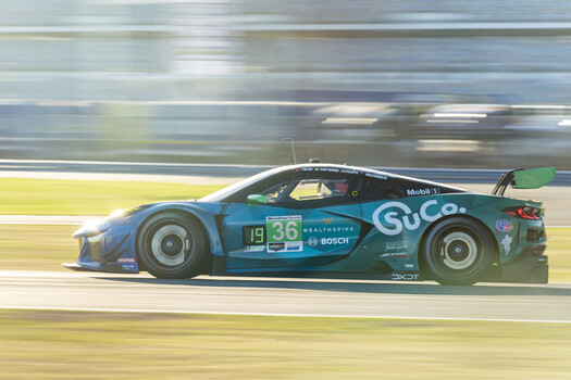Dark teal race car with number 36 racing on track with motion blur