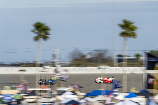 Motion-blurred racing cars competing on an oval track with grandstands and palm trees
