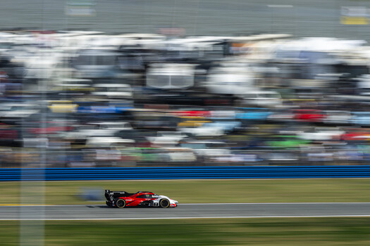 Red race car on track with motion blur and grandstand in background