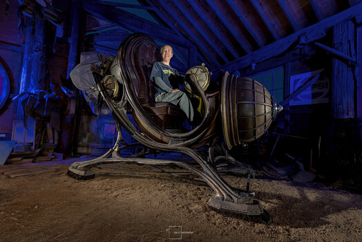 Mannequin seated inside illuminated spherical metal sculpture with blue ambient lighting