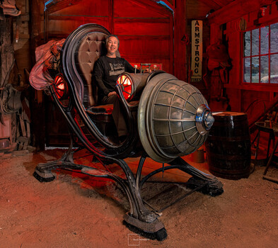 Person posing inside a large vintage red industrial lamp fixture in a red-walled studio space