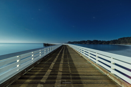 Long wooden pier with white railings extending toward the horizon over calm blue water