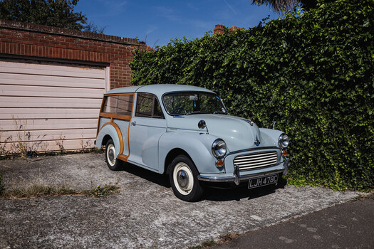 Light blue vintage Morris Minor car with wood-paneled sides parked in driveway