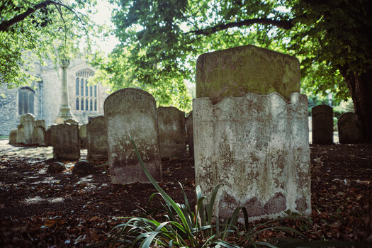 Weathered headstones in a shaded cemetery with a stone church visible in the background