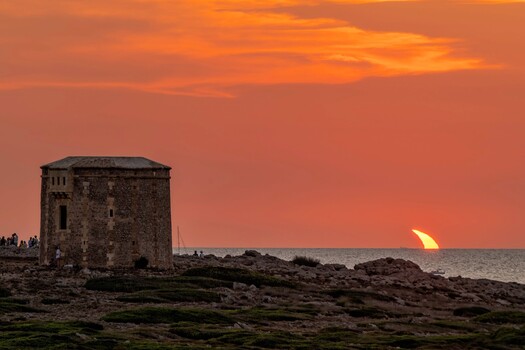 Ancient stone tower on rocky coastline during golden hour sunset