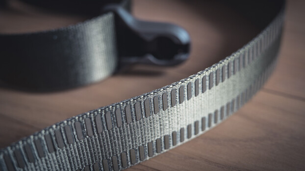 Close-up macro shot of white webbing straps with metal buckles and fasteners on wooden surface