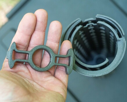 Hand holding an ornate brass or bronze coupling device next to a circular opening