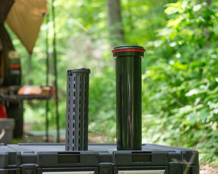 Two cylindrical lens hoods mounted on a camera rail system with forest background