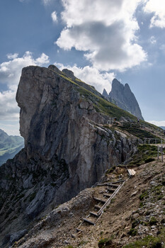 Steep wooden staircase carved into dramatic limestone cliff face with alpine valley view below