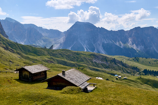 Alpine valley with dark wooden chalets and dramatic mountain peaks under blue sky with clouds