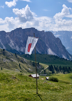 Austrian flag hanging from pole in alpine meadow with dramatic mountain peak and clouds