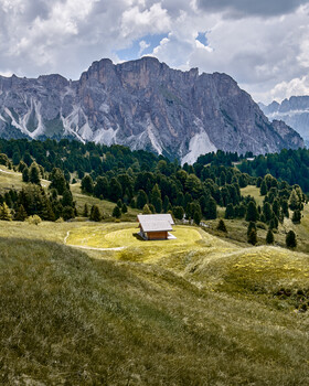 Alpine mountain landscape with isolated wooden chalet nestled in verdant meadow beneath dramatic peaks