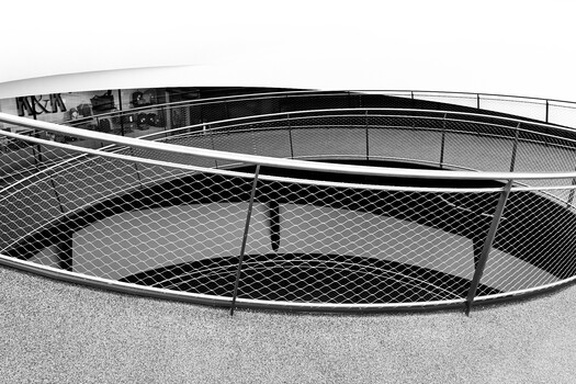 Black and white photograph of overlapping curved metal structures with mesh netting and railings