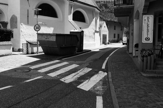 Black and white street scene with zebra crossing, parked truck, and Mediterranean architecture