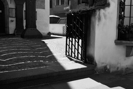 Black metal lattice gate casting geometric shadow on sunlit courtyard pavement