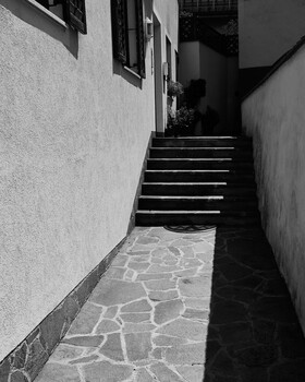Narrow stairwell with white walls and dark stairs leading upward between textured stone paving