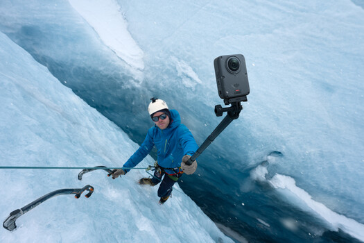 Ice climber on glacier using ice axes with action camera mounted on selfie stick