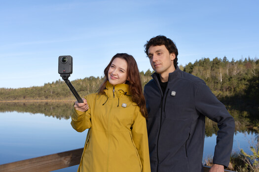 Two people taking a selfie with an action camera on a wooden dock overlooking a calm lake