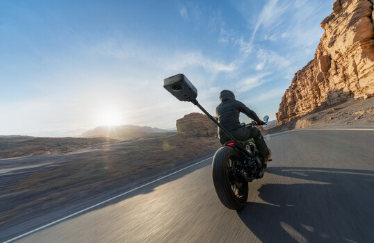 Motorcycle rider leaning into a curve on a desert highway at sunset, rocky cliffs visible on both sides
