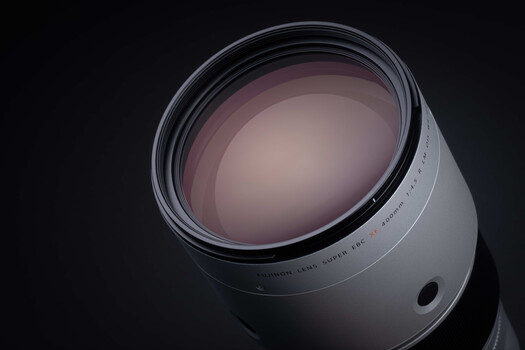 White telephoto lens with purple-tinted glass elements against dark background