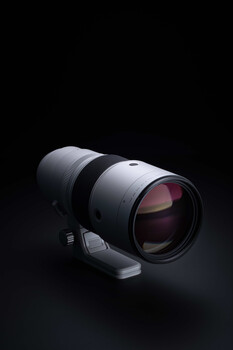 White telephoto lens with pink-tinted optics mounted on a dark background