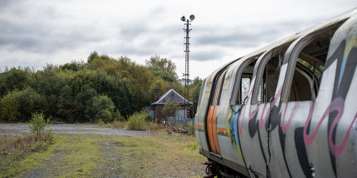 Modern commuter train with colorful livery parked beside rural landscape with communication tower