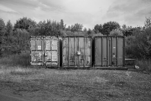 Row of weathered industrial shipping containers in a rural overgrown field