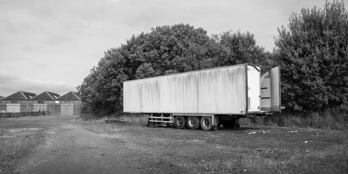 White commercial delivery truck parked on gravel near residential houses and trees