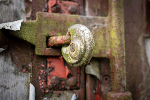 Weathered circular metal latch covered in moss and rust on corroded industrial machinery