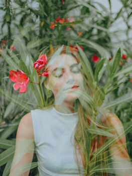 Woman with eyes closed surrounded by red flowers and green foliage in double exposure composite
