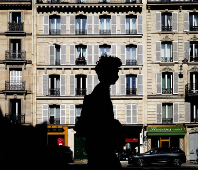 Silhouetted figure in profile against Haussmann-style Parisian apartment building facade