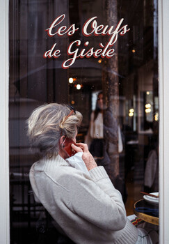 Elderly woman in profile viewing storefront window with neon script signage