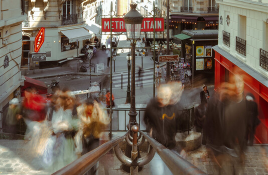 Parisian street scene with blurred pedestrians and Metro sign, shot from elevated perspective