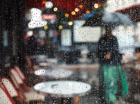 Raindrop-covered glass with blurred street scene and warm holiday lights behind