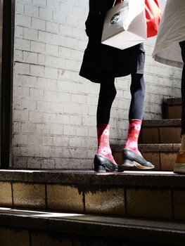 Person in athletic wear standing on a ledge against a white brick wall, wearing pink and gray socks